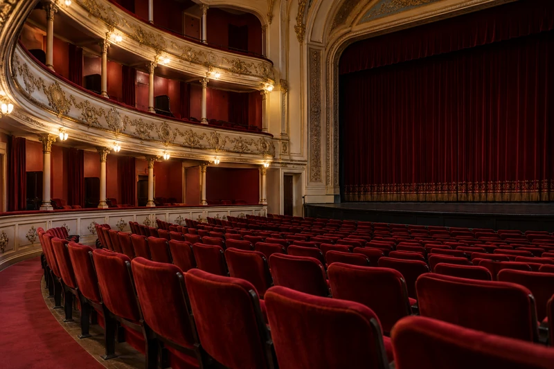 Butacas rojas y balcones de una sala de teatro histórica vacía.